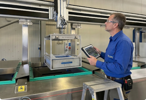 Technician operating ultrasonic cleaning process with industrial cleaning bath and control panel.